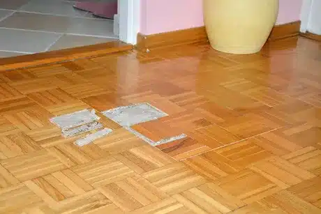 Damaged parquet flooring with missing pieces and visible adhesive, indicating the need for repair or replacement.